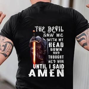 May include: A black t-shirt with a graphic of a knight kneeling with a sword. The text on the shirt reads "The Devil Saw Me With My Head Down And Thought He'd Won Until I Said Amen."