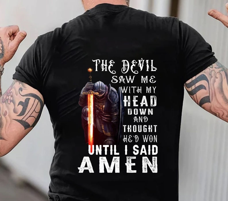 May include: A black t-shirt with a graphic of a knight kneeling with a sword. The text on the shirt reads "The Devil Saw Me With My Head Down And Thought He'd Won Until I Said Amen."