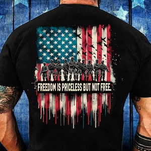 Puede incluir: Camiseta negra con un gráfico de una bandera estadounidense y soldados con el texto "Freedom is priceless but not free."