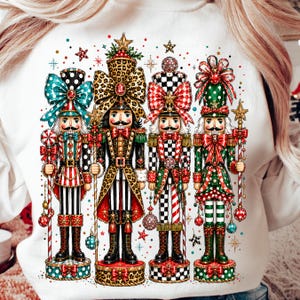 Könnte beinhalten: Ein weißes Sweatshirt mit einem Grafikdruck von vier Nussknacker-Figuren. Jeder Nussknacker trägt eine Uniform mit verschiedenen Mustern und großen Schleifen, hält einen Stab und steht auf einem runden Sockel, umgeben von kleinen Sternen und Punkten.