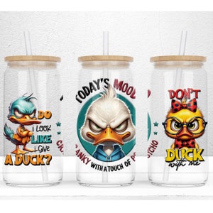 May include: Three glass tumblers with bamboo lids and straws. Each tumbler features a cartoon duck with a different saying. The first tumbler says "Do I look like I give a duck?" The second tumbler says "Today's mood: Cranky with a touch of psycho." The third tumbler says "Don't duck with me."