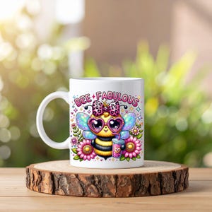 May include: White ceramic mug featuring a cartoon bee with heart-shaped sunglasses, a bow, and wings. The mug has the words "BEE FABULOUS" and is surrounded by flowers. The mug is on a wooden slice.