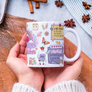 Pode incluir: Caneca de cer&acirc;mica branca com ilustra&ccedil;&otilde;es coloridas e texto. A caneca apresenta as palavras "Science Maker" e "Remember teaching is tough but so are you." Outras ilustra&ccedil;&otilde;es incluem um arco-&iacute;ris, uma borboleta e uma ma&ccedil;&atilde;.