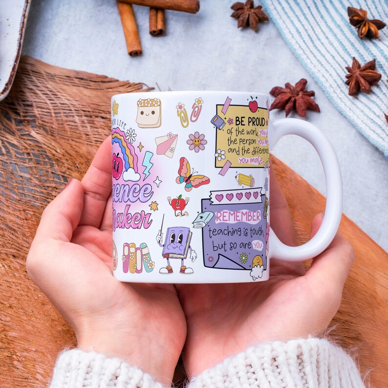 Pode incluir: Caneca de cer&acirc;mica branca com ilustra&ccedil;&otilde;es coloridas e texto. A caneca apresenta as palavras "Science Maker" e "Remember teaching is tough but so are you." Outras ilustra&ccedil;&otilde;es incluem um arco-&iacute;ris, uma borboleta e uma ma&ccedil;&atilde;.