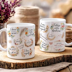 May include: Two white ceramic mugs with inspirational quotes and floral designs. One mug features phrases like "I deserve the best" and "I am strong." The other mug says "Today I will choose kindness" and "I am happy and complete."