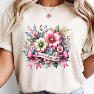 Peut inclure: Un t-shirt beige avec un motif floral et le texte "Happy Mother's Day" sur un ruban rose.