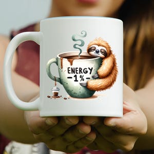 May include: White ceramic coffee mug with a light blue interior. The mug features a cartoon sloth hugging a coffee cup with the text "ENERGY -1%-". A small coffee cup and coffee beans are also depicted.