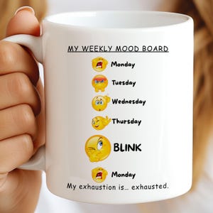 Puede incluir: Taza de cerámica blanca con el texto "MY WEEKLY MOOD BOARD" y emoticonos que representan cada día de la semana. El texto "My exhaustion is... exhausted" está en la parte inferior. La taza está sujeta por una persona.