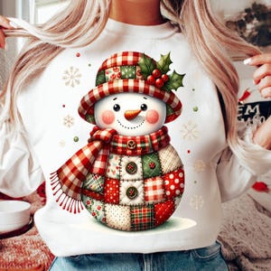 Könnte beinhalten: Weißes Sweatshirt mit einem skurrilen Schneemann-Design. Der Schneemann hat einen Patchwork-Körper, eine Karottennase und einen karierten Hut und Schal. Stechpalmen und Beeren schmücken den Hut. Dekorative Schneeflocken und Punkte sind verstreut.