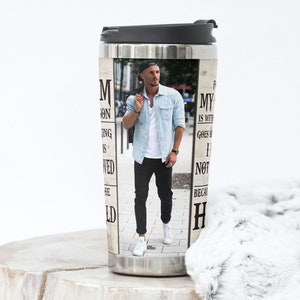 May include: Stainless steel travel mug with a black lid. The mug features a photograph of a man in a denim shirt and black pants. Text on the mug reads "M ON ING IS WED HE" and "MY IS WITH GOES I NOT BECAU H".