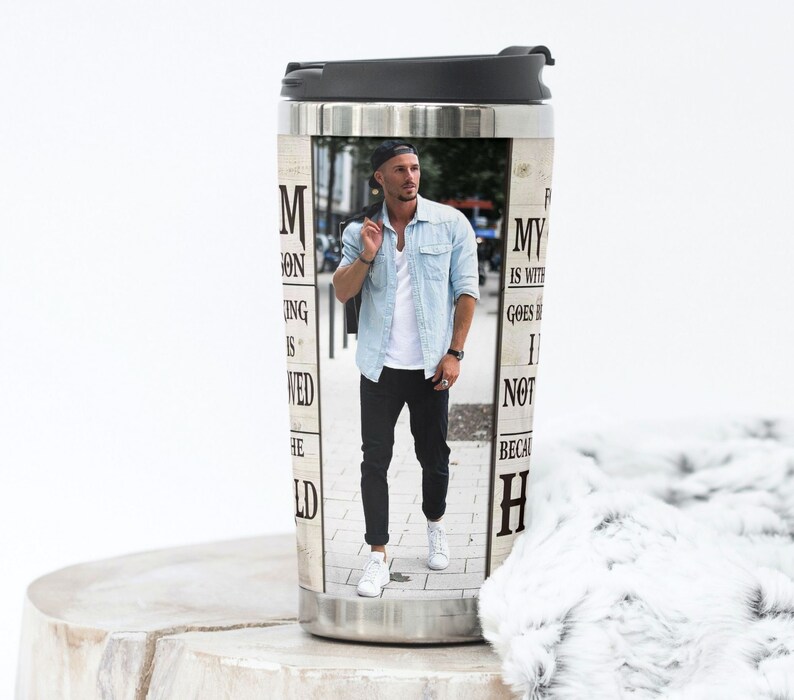 May include: Stainless steel travel mug with a black lid. The mug features a photograph of a man in a denim shirt and black pants. Text on the mug reads "M ON ING IS WED HE" and "MY IS WITH GOES I NOT BECAU H".