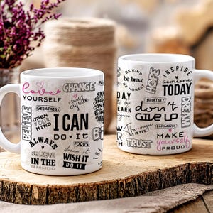 May include: Two white ceramic mugs with black and pink text. One mug says "I CAN" with other words like "Believe" and "Do It". The other mug says "Don't Give Up" and "Inspire Today". The mugs sit on a wooden surface.