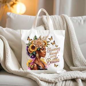May include: White tote bag featuring a digital illustration of a woman with a floral crown and butterflies. The text "Blooming through every Battle" is displayed on the bag. The bag has white handles and is made of a sturdy fabric.