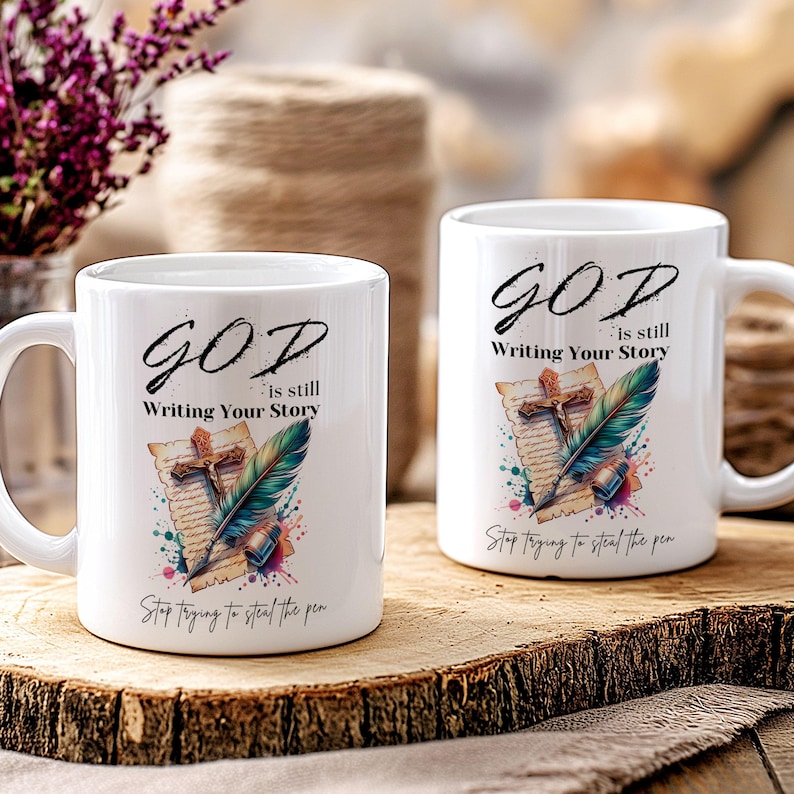 Puede incluir: Dos tazas de cer&aacute;mica blanca con un dise&ntilde;o colorido que presenta una pluma estilogr&aacute;fica, una cruz y un trozo de pergamino. El texto en las tazas dice "GOD is still Writing Your Story" y "Stop trying to steal the pen".