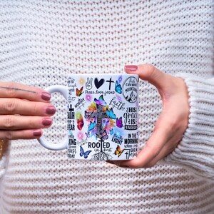 May include: White ceramic mug with a cross design, butterflies, and inspirational text. The mug features phrases such as "Peace, love, Jesus" and "His grace is enough." The design incorporates various colours and a floral theme.