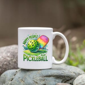 May include: White ceramic mug with a green, white, and rainbow design. The mug features a pickleball and paddle with the text "Happy People Play Pickleball".