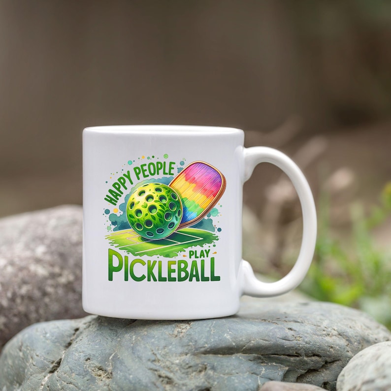May include: White ceramic mug with a green, white, and rainbow design. The mug features a pickleball and paddle with the text "Happy People Play Pickleball".