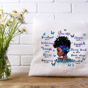 May include: A white pillow with a blue and purple design featuring a woman with an afro and butterflies. The text on the pillow reads "You are Beautiful, Victorious, Enough, Strong, Amazing, Chosen, Capable, Always Loved, Never Alone, Created" with corresponding bible verses.