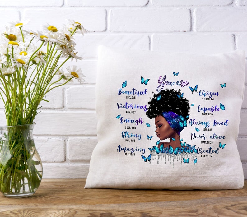May include: A white pillow with a blue and purple design featuring a woman with an afro and butterflies. The text on the pillow reads "You are Beautiful, Victorious, Enough, Strong, Amazing, Chosen, Capable, Always Loved, Never Alone, Created" with corresponding bible verses.