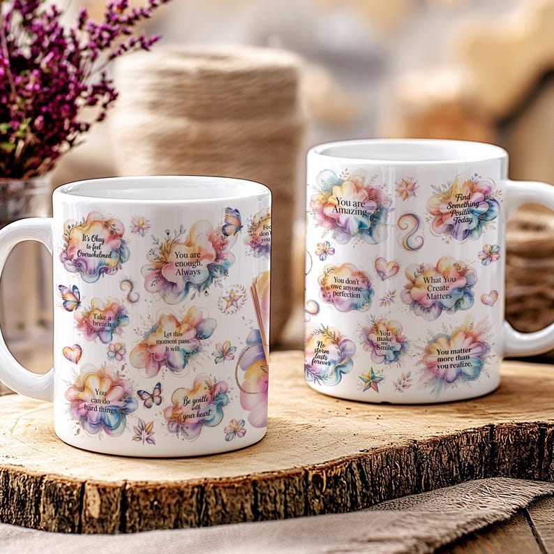 K&ouml;nnte beinhalten: Zwei wei&szlig;e Keramikbecher mit inspirierenden Zitaten und floralen Designs. Die Becher zeigen S&auml;tze wie "Du bist erstaunlich" und "Finde heute etwas Positives." Schmetterlinge und Herzen verzieren die Becher.