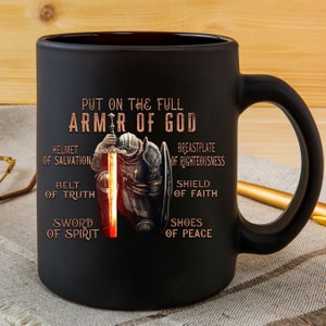 May include: Black ceramic coffee mug with a graphic of a knight in armor holding a sword. The text "Put on the full armor of God" is printed on the mug, along with the words "Helmet of Salvation", "Breastplate of Righteousness", "Belt of Truth", "Shield of Faith", "Sword of Spirit", and "Shoes of Peace".