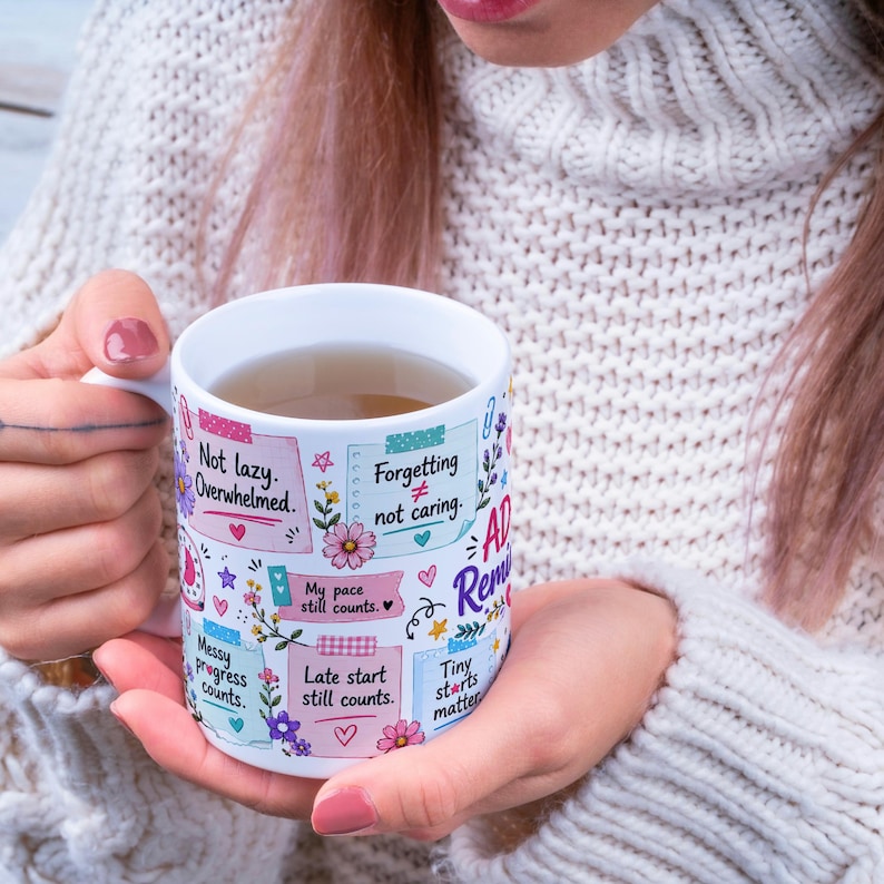May include: White ceramic mug with colorful sticky notes and floral designs. The mug has text that reads "Not lazy. Overwhelmed," "Forgetting &ne; not caring," and "Tiny starts matter." The mug is filled with a light brown liquid.