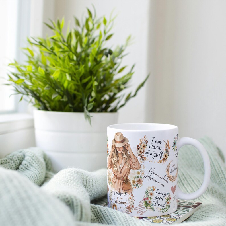 May include: White ceramic mug featuring an illustration of a woman in a hat and coat, surrounded by floral designs and text. The mug also has the phrases "I am proud of myself", "Happiness looks gorgeous on me", "I am a good friend", and "I support my dreams".