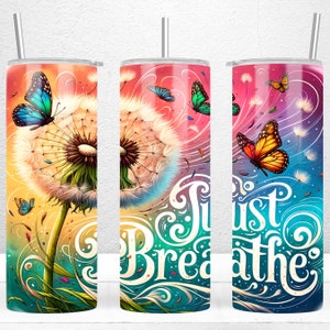 Può includere: Un bicchiere in acciaio inossidabile colorato con un design di dente di leone e farfalle. Il bicchiere ha le parole "Just Breathe" in un font stilizzato.