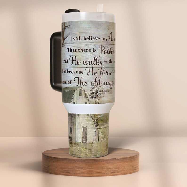 May include: A large white and black tumbler with a handle, straw, and lid. The tumbler features a rustic design with a barn and windmill image, and text that reads "I still believe in America...He walks with me...He lives...The old rugged".