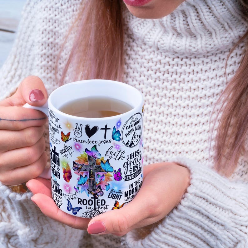 May include: White ceramic mug with a handle, decorated with a cross, butterflies, and inspirational text. The mug contains a light-coloured liquid. The design includes the words "Peace, love, jesus", "Faith can move mountains", and "Rooted in Christ".