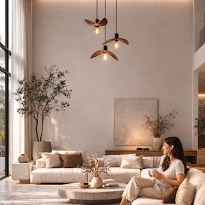 May include: A modern living room featuring a beige sofa, a round coffee table, and a large window. Three pendant lights with wooden shades hang from the ceiling. The room is decorated with neutral tones and natural elements.