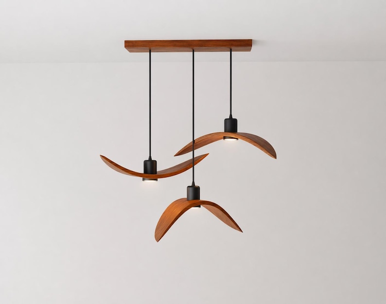 May include: A modern, three-light pendant lamp with a rectangular wooden canopy. Each light features a curved, wooden shade with a black fixture and a small, integrated LED light. The design is minimalist and elegant, suitable for various interior styles.