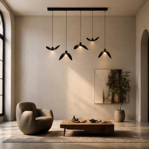 May include: Modern black pendant lights with a unique, leaf-like design hang from a black rectangular fixture. The lights are suspended above a living room with a neutral color palette, a brown armchair, and a wooden coffee table.