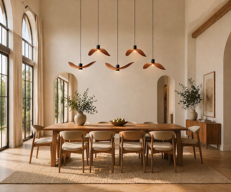 May include: A modern dining room featuring a large wooden table with eight chairs. Above the table, five pendant lights with wooden shades hang from the ceiling. The room has a neutral color palette with a rug and large windows.
