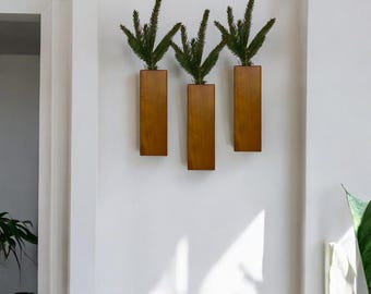 May include: Three wooden wall planters with green plants in them. The planters are mounted on a white wall.