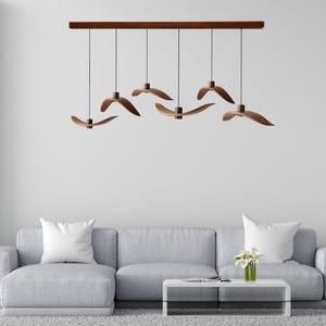 Puede incluir: Una lámpara colgante moderna de madera con seis pantallas de madera curvadas que cuelgan de una sola barra de madera. Las pantallas están dispuestas en forma escalonada, creando un diseño dinámico e interesante.