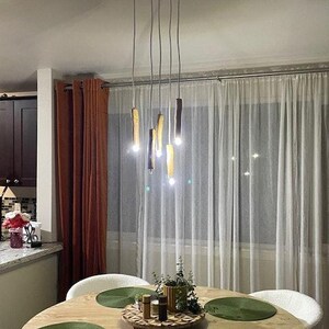 Może przedstawiać: Drewniana lampa sufitowa z pięcioma żar&oacute;wkami wiszącymi z niej. Lampa znajduje się w jadalni z drewnianym stołem i zielonymi podkładkami.