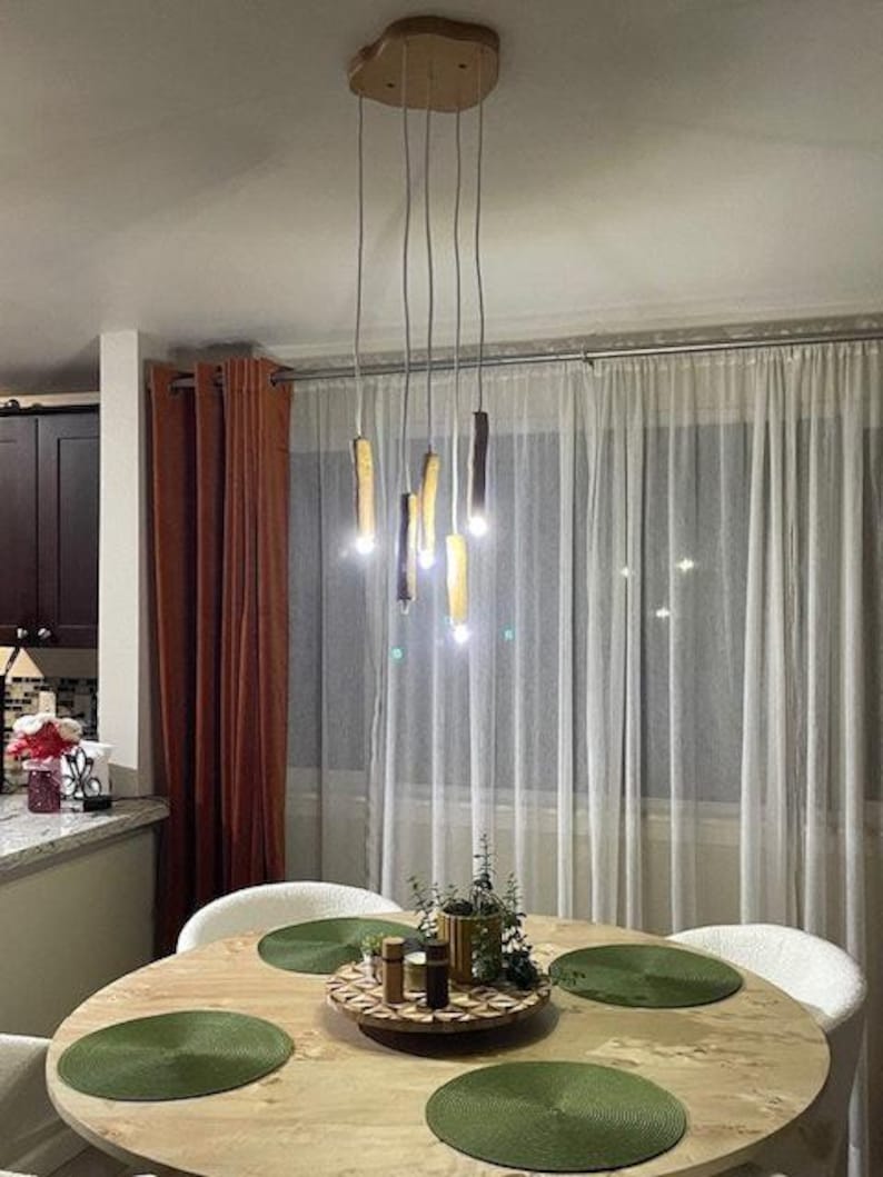 Może przedstawiać: Drewniana lampa sufitowa z pięcioma żar&oacute;wkami wiszącymi z niej. Lampa znajduje się w jadalni z drewnianym stołem i zielonymi podkładkami.
