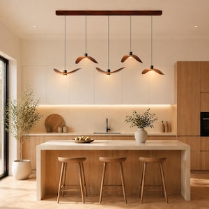 May include: A modern kitchen with a light wood island and matching stools. Above the island, five pendant lights with wooden shades hang from a dark wood beam. The kitchen features light-colored cabinets and a large window.