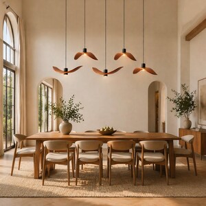 May include: A modern dining room featuring a large wooden table with eight chairs. Above the table, five pendant lights with wooden shades hang from the ceiling. The room has a neutral color palette with a rug and large windows.