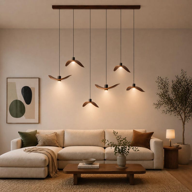 May include: A modern living room featuring a cream-colored sectional sofa, a wooden coffee table, and a series of six pendant lights with wooden shades. The lights are suspended from a dark brown rectangular fixture. A framed abstract art piece hangs on the wall.