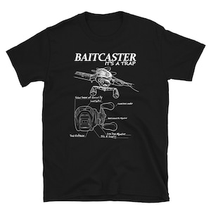 May include: Black t-shirt with a white illustration of a baitcaster fishing reel and the text "Baitcaster It's a Trap!" The illustration shows the different parts of the reel with labels like "False Sense of Security", "Line Time Adjuster", and "Top Release".