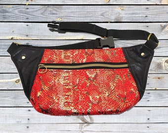 May include: A red and gold snakeskin patterned fanny pack with a black leather flap and a black adjustable strap with a buckle.