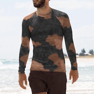 Peut inclure: Un homme portant une chemise à manches longues avec un motif camouflage brun et noir et un short brun foncé marche sur une plage de sable.