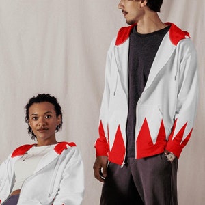 May include: Two people wearing white and red jackets with a jagged pattern. The person on the left is sitting on a chair and the person on the right is standing.