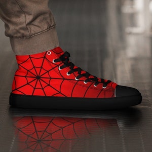 May include: Red high-top canvas shoes with a black spider web design. The shoes have black laces and a black rubber sole.