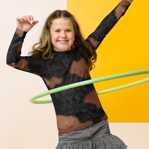 May include: A young person wearing a brown and black tie-dye long-sleeved shirt, a denim skirt, and black leggings with a snake print. They are holding a green hula hoop in front of them.