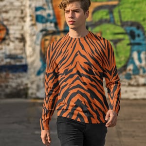 Op de afbeelding: Een shirt met lange mouwen met een oranje en zwart tijgerstreepdessin. Het shirt is gemaakt van een zacht, comfortabel materiaal en heeft een ontspannen pasvorm.