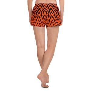 Puede incluir: Un par de pantalones cortos deportivos naranja y negro con un estampado de cebra. Los pantalones cortos se muestran en una modelo desde la parte posterior.