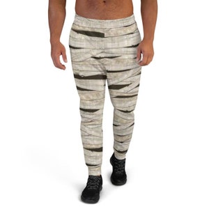 May include: A pair of sweatpants with a mummy-inspired print. The sweatpants are a light beige color with brown bandages printed on them. The sweatpants have a drawstring waistband and a relaxed fit.
